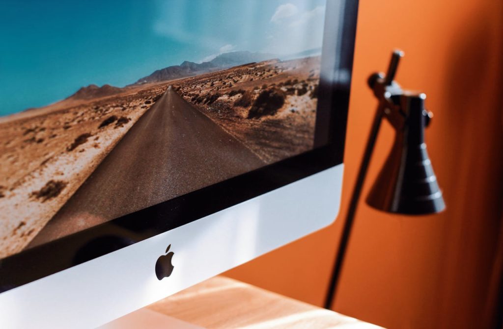 Image d'un ordinateur iMac posé sur un bureau avec un fond peint en orange.