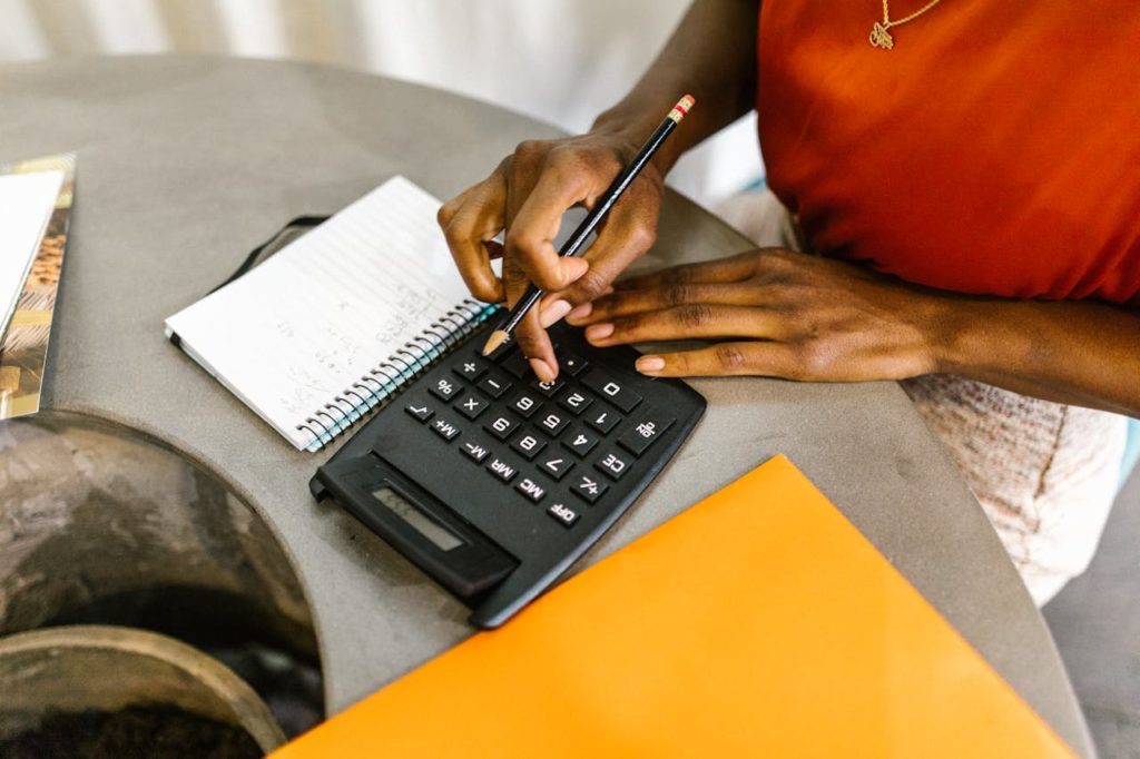 Femme noire en train de calculer avec une calculatrice quel budget elle peut allouer au marketing de son entreprise.