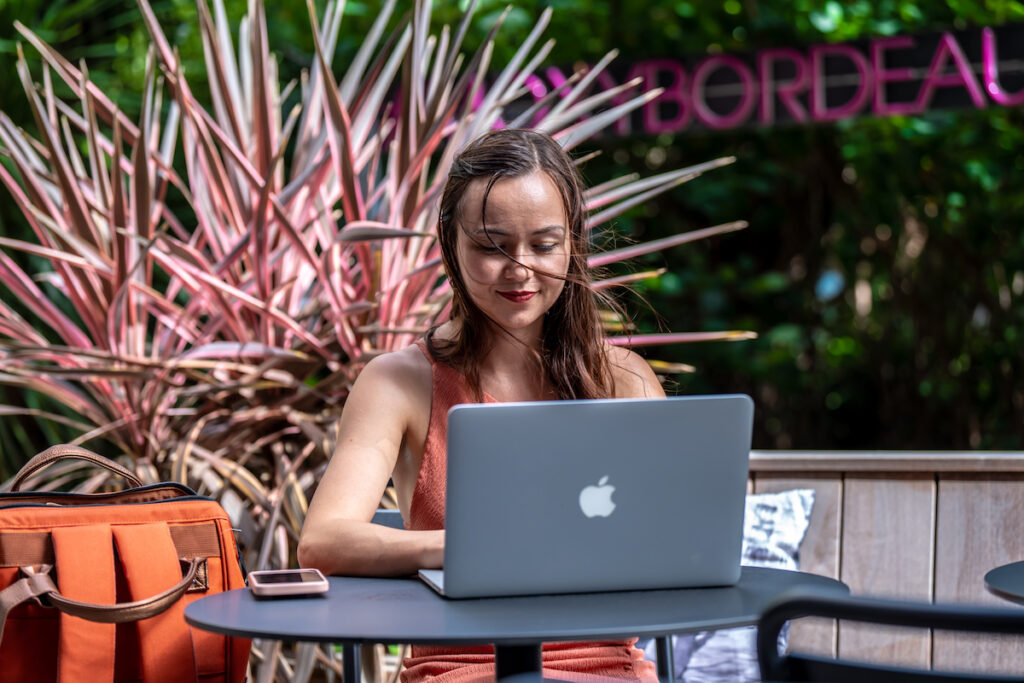 Photo d'Alexia Peytoureau assise sur une terrasse en train de définir une stratégie éditoriale derrière son ordinateur.