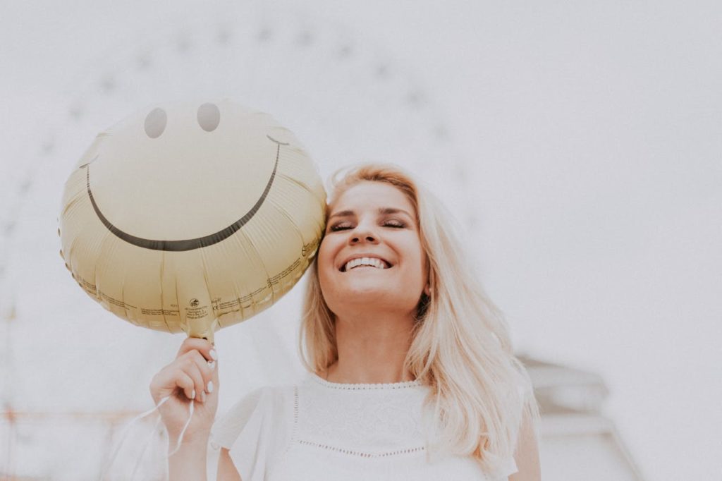 Jeune femme blonde souriante avec un ballon smiley dans la main droite