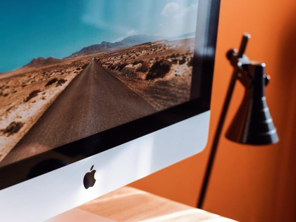 Image d'un ordinateur iMac posé sur un bureau avec un fond peint en orange.