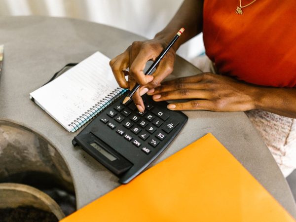 Femme noire en train de calculer avec une calculatrice quel budget elle peut allouer au marketing de son entreprise.