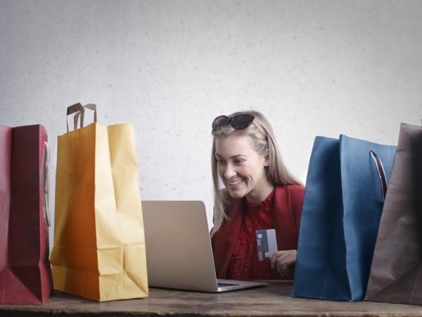 Jeune femme en train de passer des commandes depuis son ordinateur portable, entourée de sacs en papier de couleur.