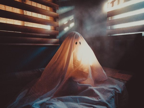 Une personne déguisée en fantôme assise sur un lit dans la pénombre.