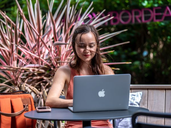 Photo d'Alexia Peytoureau assise sur une terrasse en train de définir une stratégie éditoriale derrière son ordinateur.
