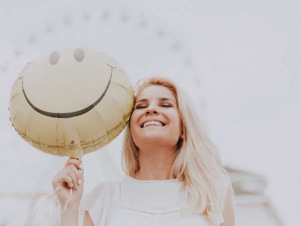 Jeune femme blonde souriante avec un ballon smiley dans la main droite